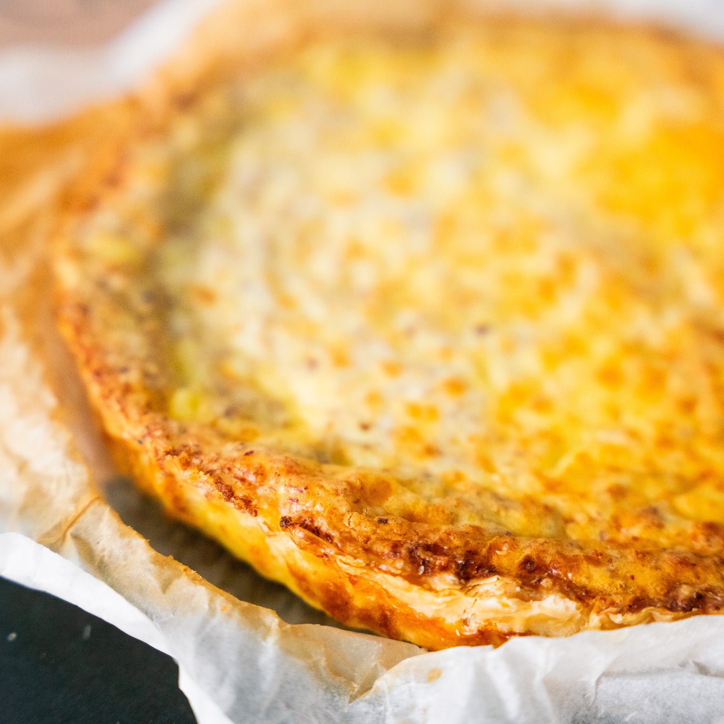 Close-up form a classic quiche Lorraine with a golden, flaky crust and a rich, creamy filling, baked to perfection. Presented in parchment paper, the quiche exudes a warm and inviting appearance, ready to be served