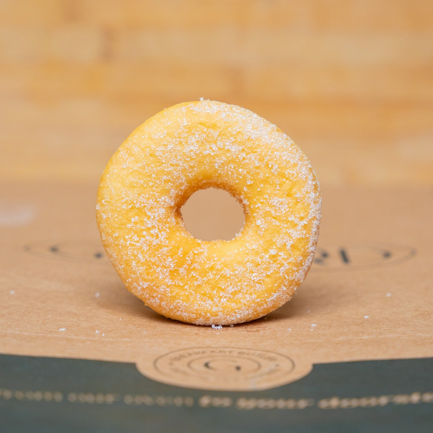 Close-up of a golden sugar-coated donut on a rustic surface, perfect for breakfast or dessert lovers.