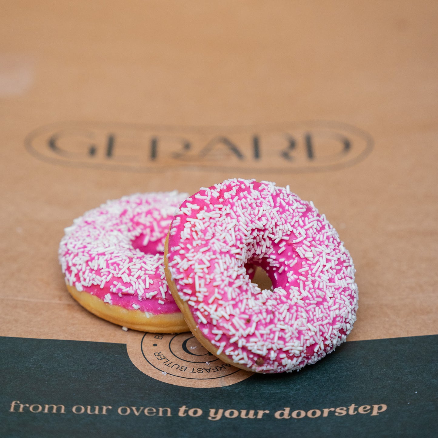 Two bright pink donuts topped with white sprinkles, placed on a natural brown background, showcasing its vibrant color and delicious texture