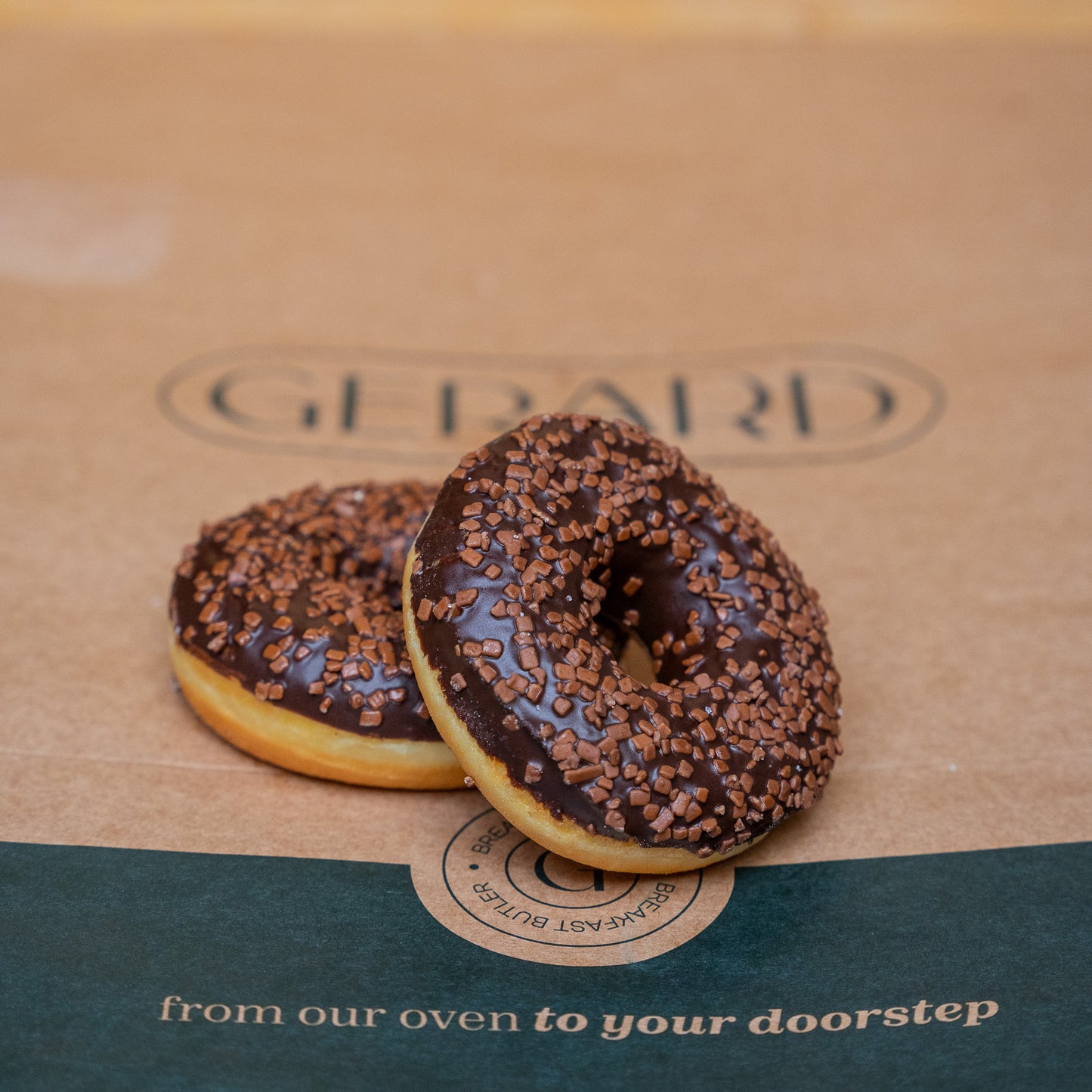 Two rich chocolate donuts covered with chocolate sprinkles, placed on a natural brown background, highlighting its indulgent and textured topping