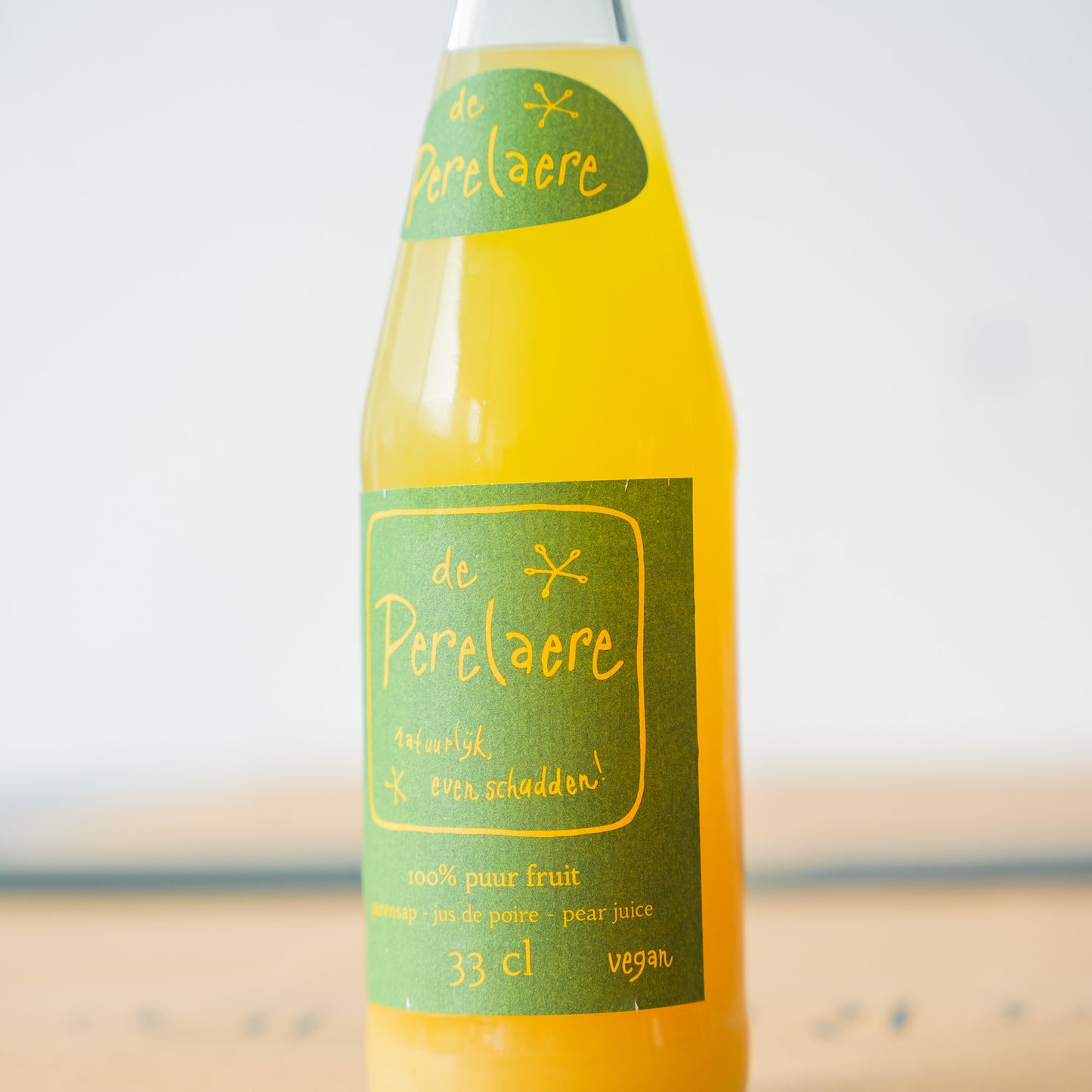 A close-up from De Perelaere pear juice bottle, showcasing its vibrant green and yellow label, filled with 100% pure fruit juice for a refreshing taste
