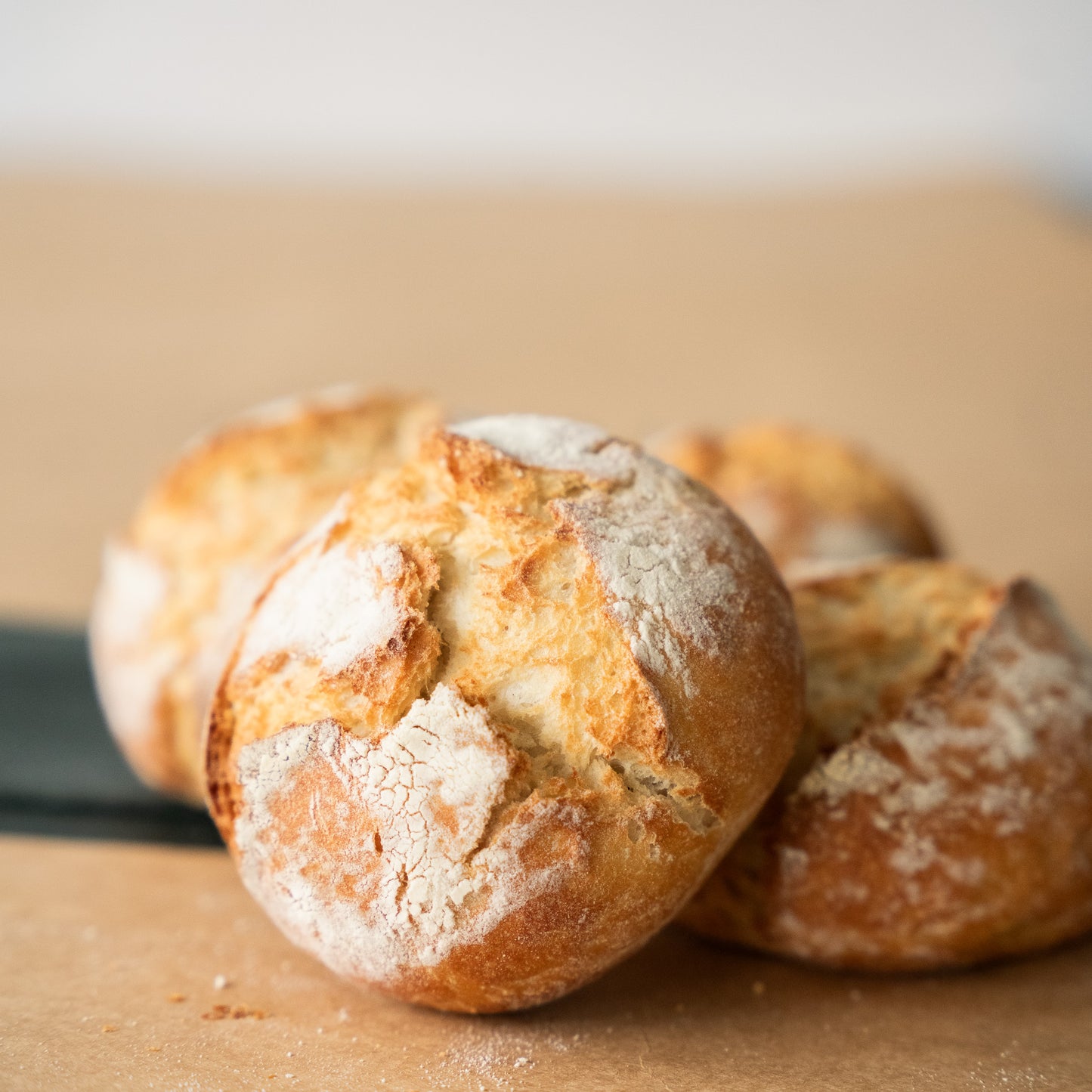 Close-up of freshly baked crusty bread rolls with a golden, crackly exterior, dusted lightly with flour, sitting on a wooden surface