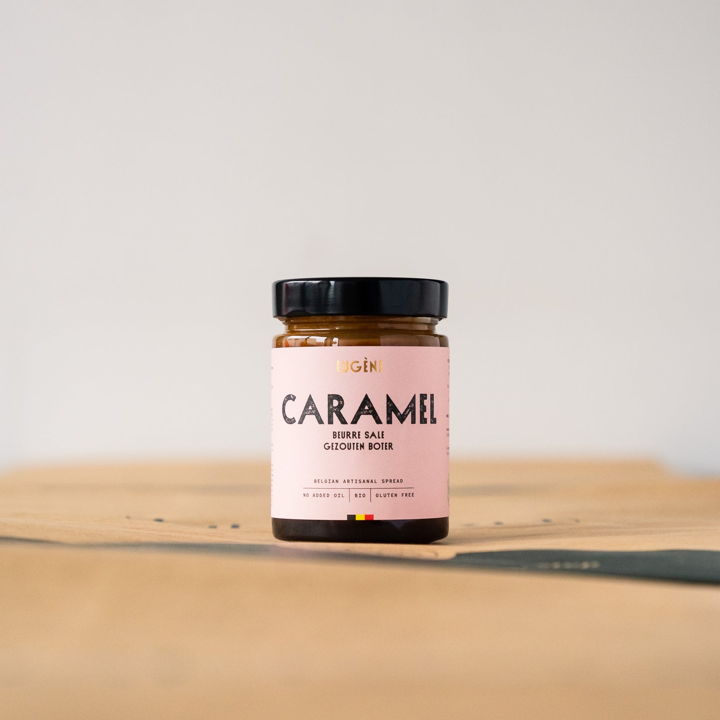 Jar of handcrafted salted caramel butter made with Belgian fresh cream, cane sugar, farm butter, and Guérande salt, placed on a rustic wooden surface.