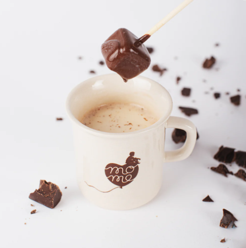Choc-o-lait milk chocolate stick melting in a cup of hot milk, surrounded by chocolate shavings for a delicious and creamy treat