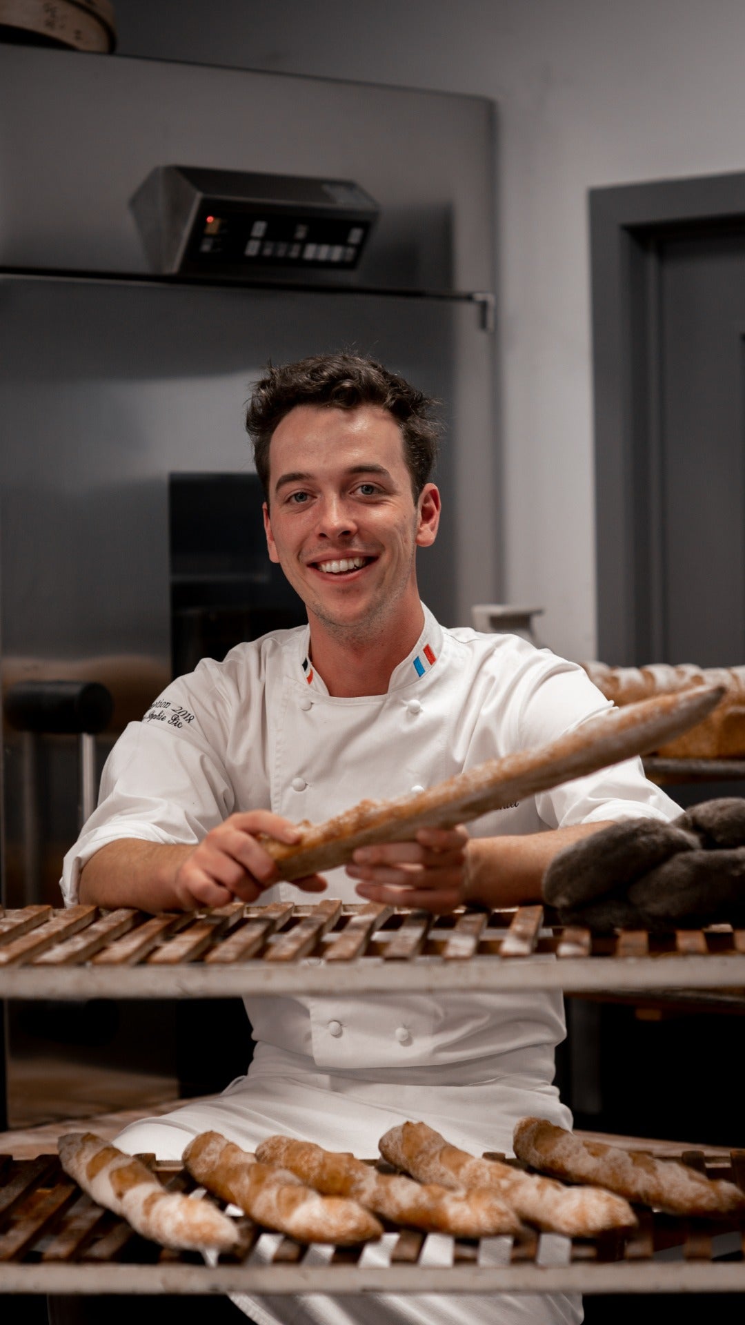 Picture of Master Chef Sébastien in his chef suit while holding one of its creations, namely a baguette tradition.