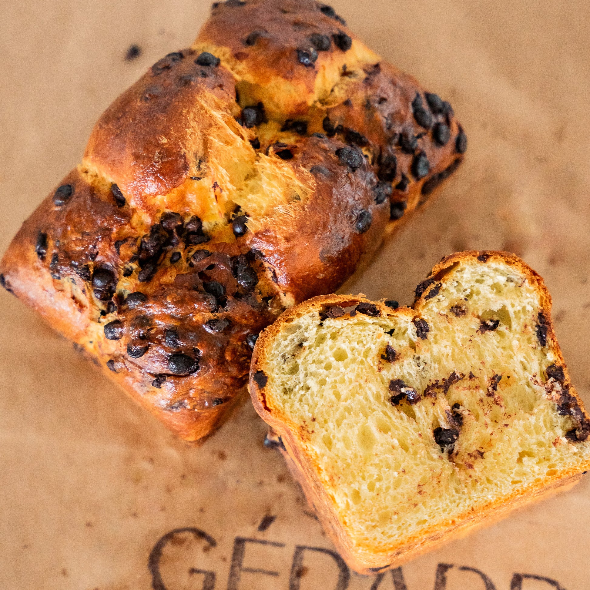A Chocolate Brioche with lots of chocolate chips on top next to a loaf of Chocolate Brioche.