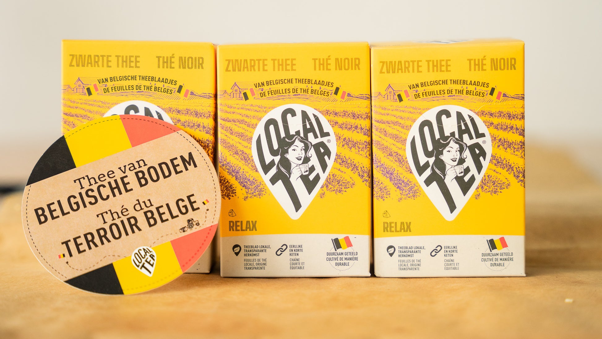 Three lavender-black tea packages placed next to each other with the writing "Tea from Belgian territory".