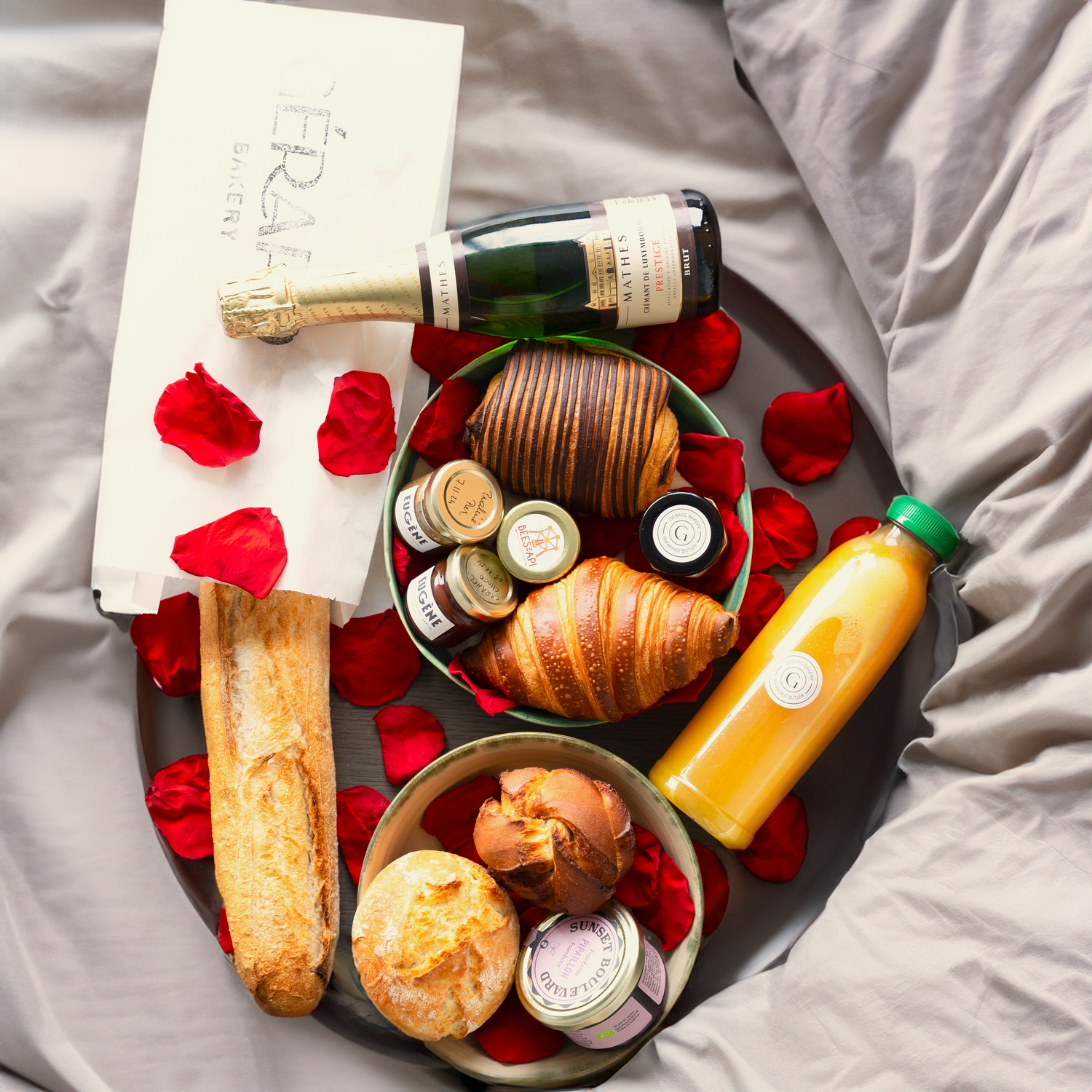 Romantic breakfast basket with croissants, baguette, orange juice, sparkling wine, and roses, perfect for Valentine's Day.