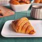 A plate with a freshly baked croissant, golden and flaky, arranged neatly on a white plate.