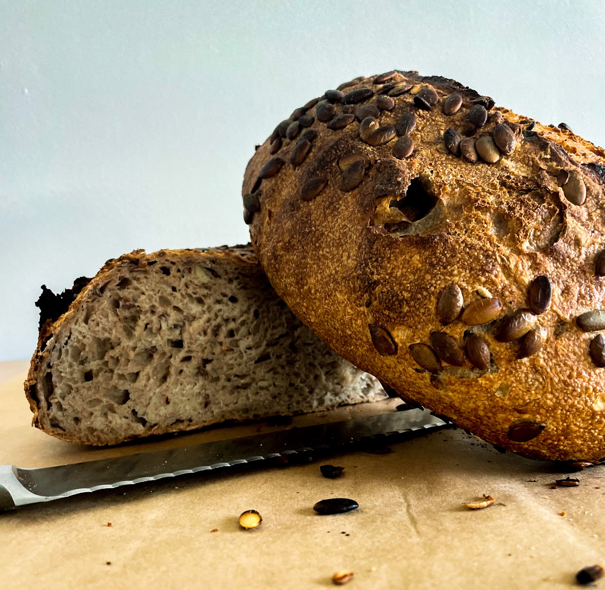 A pumpkin sead bread that is cut in two with a knife laying next to it