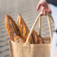 A hand which holds a bag filled with Gérard sourdough baguettes.