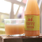 A pear and ginger juice bottle from Toffe Peren laying next to a glass filled with pear and giner juice